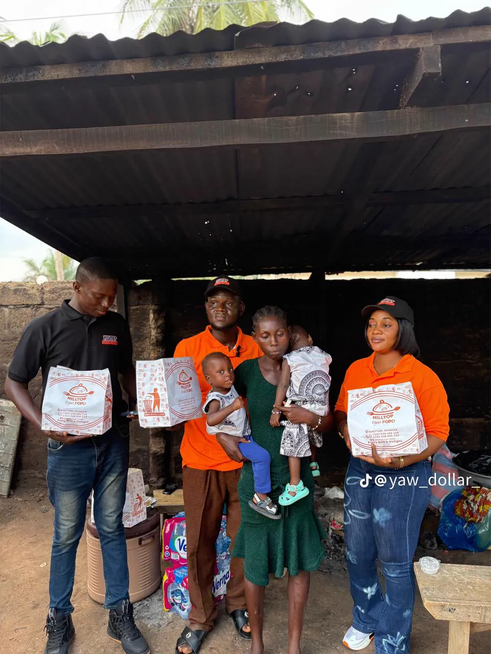 Volunteers holding food packs beside a mother carrying two young children