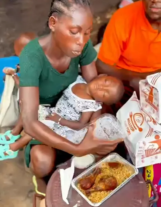 A mother holding her child while receiving a meal